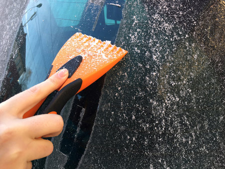 Female hand holding an ice-scraper to scrape ice from the windshield in winter