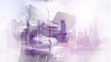 double exposure image of a business man using a tablet device during sunrise overlay with cityscape image. modern life and business conceptの写真素材