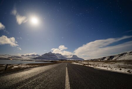 straight country road under the moonlight with dramatic clouds and starry sky, Icelandの写真素材