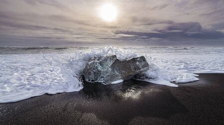 wave crashing on an iceberg on black lava sand beach near JÃ¶kulsÃ¡rlÃ³n Glacier Lake, Icelandの写真素材