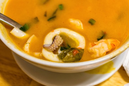 Thai soup Tom Yam with seafood in bowl on table in cafe with spoon close-up tastyの写真素材