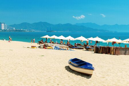 NHA TRANG, VIETNAM - APRIL 11 2019: Plenty loungers and parasols on sandy beach and boat near ocean for relaxのeditorial素材