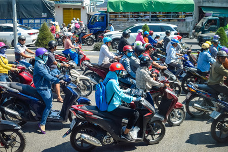 NHA TRANG, VIETNAM - APRIL 13, 2019: Plenty motorcyclists drive on road in rush hour on sunny day