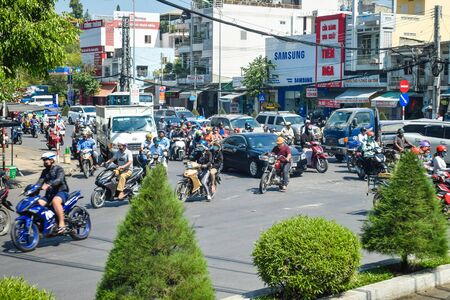 NHA TRANG, VIETNAM - APRIL 13, 2019: Plenty motorcyclists drive on road with bushes in rush hour on sunny dayのeditorial素材