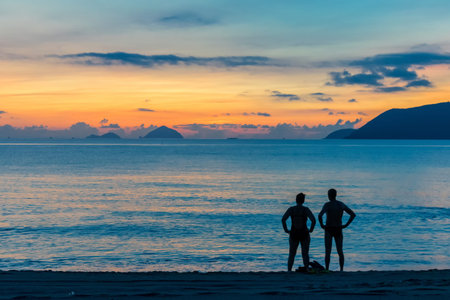 Silhouettes of two people on the beach near the sea at a colorful sunrise