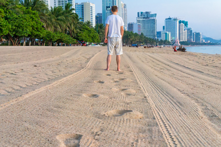 Man goes away on beach and he leaves footprints on sand at dawnの写真素材