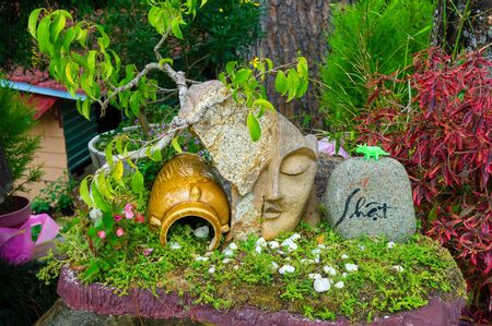 An ancient jug and a sculpture of a face near the flowers in parkの写真素材