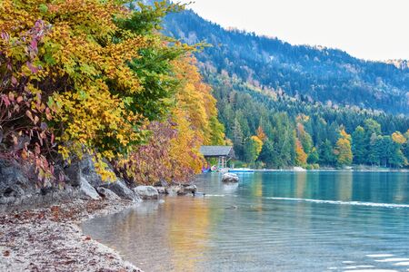 Wooden hut with boats on the lake in the autumn forest in the morning in Alpsの写真素材