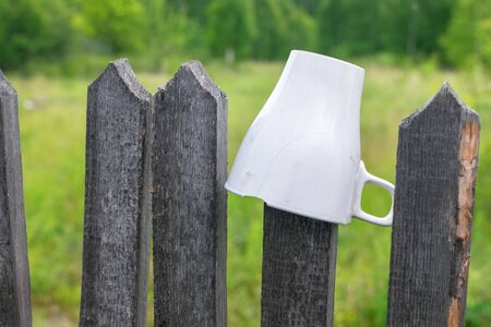 Cracked white mug with a handle on a wooden fence in gardenの写真素材