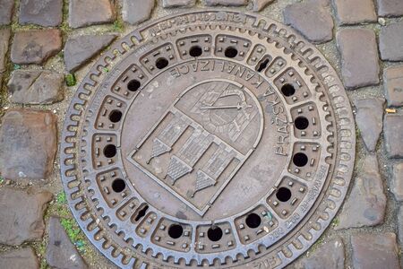 Metal sewer hatch with coat of arms in cobblestones title Prague Sewerageの写真素材