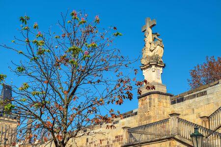 Tree without leaves and statue with a cross under bridge in Prague in autumnの写真素材