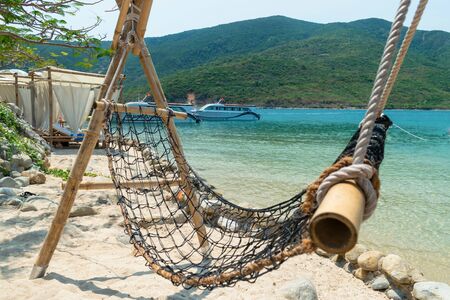 Mesh and bamboo hammock on a sandy beach and a yacht at sea in tropicsの写真素材