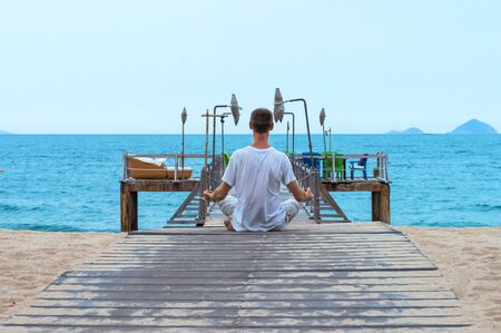 Young man meditates on wooden pier on the beach in the tropics.の写真素材
