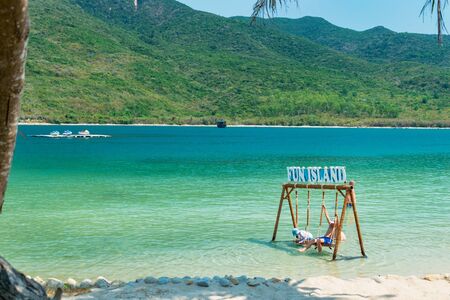 Tourists on swing in water on a sandy beach with transparent water in the tropicsの写真素材