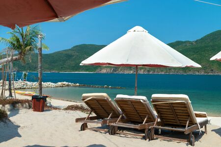 Sunbeds under parasol on a sandy beach in the tropics and blue water in the seaの写真素材