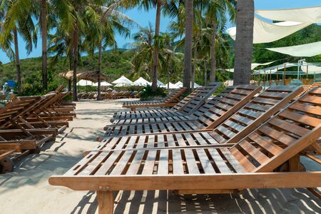 A row of wooden sunbeds on beach in the shade in the tropics under palm treesの写真素材