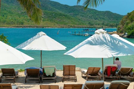 White sun umbrellas and sunbeds on the beach by the shore and blue seaの写真素材