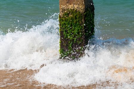 Concrete pillar with green moss and splashing waves in seaの写真素材