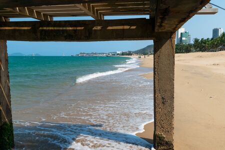 View of a sandy beach with waves and foam from under a wooden platformの写真素材