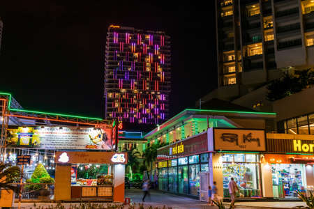 NHA TRANG, VIETNAM - APRIL 20, 2019: Glowing shop windows and cafes and skyscraper at night on street.のeditorial素材