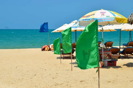NHA TRANG, VIETNAM - APRIL 21, 2019: Green flags in row on sandy beach and sun umbrellas by seaのeditorial素材