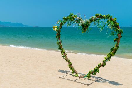 Heart-shaped wooden arch with curly flowers for beach wedding near the seaの写真素材