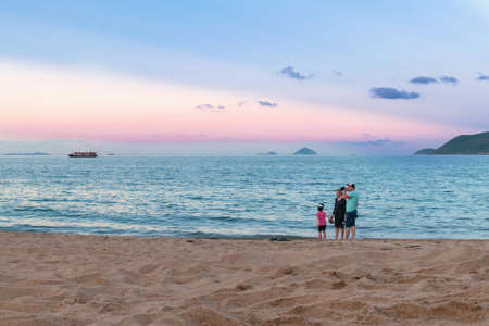 NHA TRANG, VIETNAM - APRIL 21, 2019: Family with a child by the sea on beach and pink sunset.のeditorial素材
