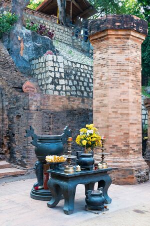 Buddhist altar with candles and bananas and flowers on table in temple with red bricksの写真素材