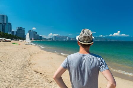 A man in a wicker hat from the back on sandy beach and boat with sailの写真素材