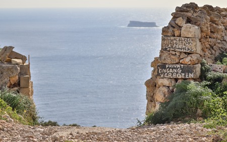Entrance with private and no entrance (Eingang Verboten) lettering on Dingli Cliffs with the Maltese Island Filfla in the backgroundの写真素材