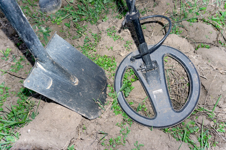 Metal detector coil over a metal object protruding from the ground. A shovel driven into the ground in the background.の写真素材