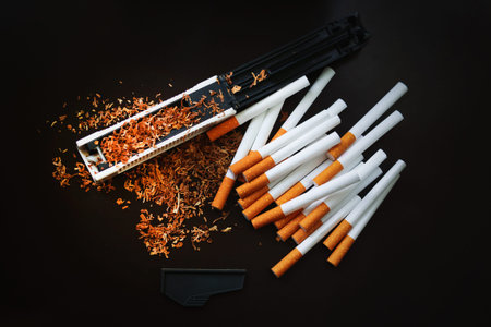 Production of cigarettes at home. The machine for cigarettes, tobacco scattered on a black...