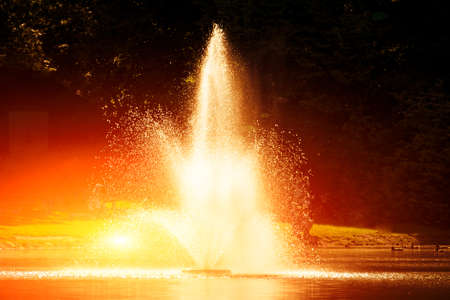 A small fountain in the lake. Against the backdrop of treesの写真素材
