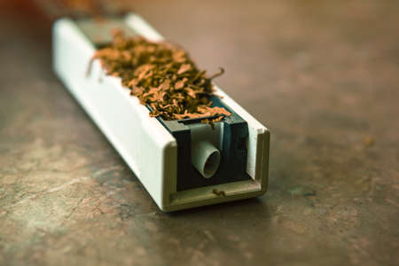 The machine for stuffing cigarettes with tobacco. Empty sighety. Rossypany tobacco on the table. Homemade cigarette productionの写真素材