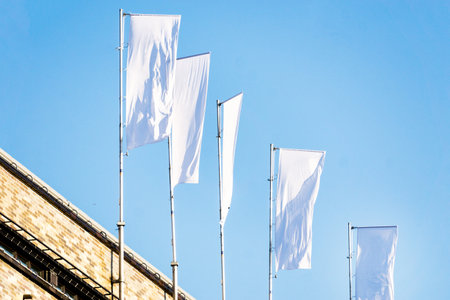 Three blank white flags on flagpoles against cloudy blue sky with perspective, corporate flag mockup to ad logo, text or symbol, company identity flag template with copy spaceの写真素材