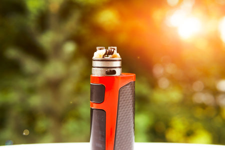 electronic cigarette on the background of trees, visible spiral wool and steam. Coil cleaning.の写真素材