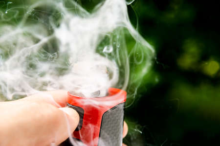 electronic cigarette on the background of trees, visible spiral wool and steam. Coil cleaning.の写真素材