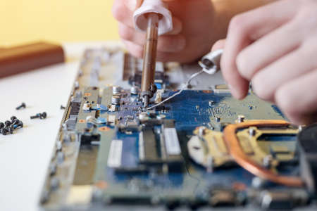 A man repairs a laptop, disassembles a laptop on a white background, solders the laptop motherboardの写真素材
