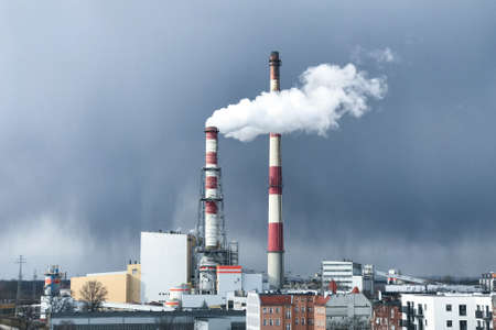 Thick white smoke comes out of a large chimney of an industrial facility or factory. Chimney against the blue sky. Environmental pollutionの写真素材