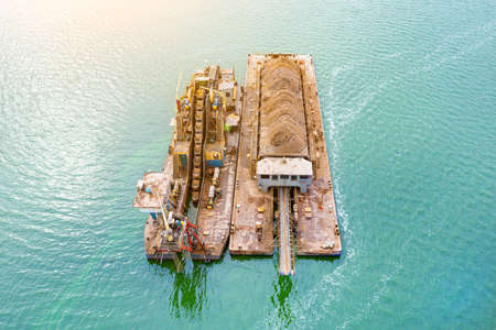Extraction of sand from the river, excavator digs out sand from the bottom of the lake and unloads it on a floating barge, miningの写真素材