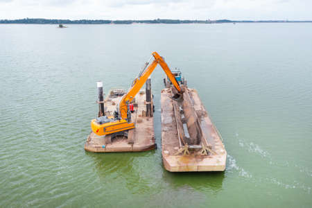 Extraction of sand from the river, excavator digs out sand from the bottom of the lake and unloads it on a floating barge, miningの写真素材