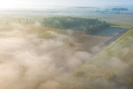 Aerial view of foggy autumn field and forest landscape. View of a small village in the morning, droneの写真素材
