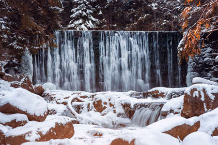 A waterfall in the winter forest and many stones covered with snow. Winter landscapeの写真素材