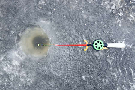 Winter fishing, fishing rod with a fishing line near the ice hole. ice with snowの写真素材