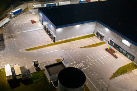Aerial view of a warehouse of goods at night. Many warehouses and trucks with trailers are in the parking lot, waiting to be loaded for further distribution of goods around the country.の写真素材