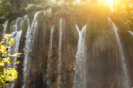 Close-up of a waterfall flowing through the rocks, illuminated by the bright rays of the sunの写真素材