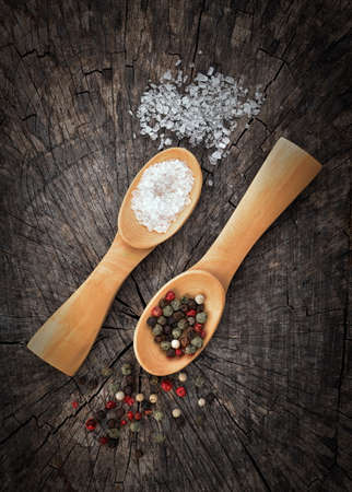 Wooden  spoons filled with salt crystals and color peppercorns. On old wooden background. Vintage effect image.の写真素材