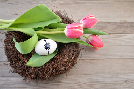 Easter eggs in a nest with tulips on a wooden background.