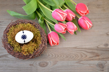 Easter eggs in a nest with tulips on a wooden background.