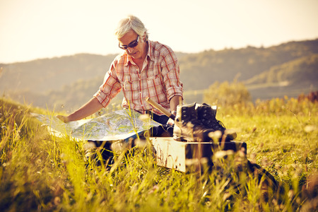 Man with map and shoes sitting in meadowの写真素材